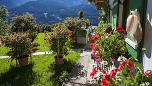 A balcony with potted plants and flowers, overlooking a mountainous landscape. - Ferienwohnung "Beim Sepperl" im Zuhäusl, 1-2 Personen, 40 qm, Dusche/WC, Südbalkon, TV, 1 Schlafzimmer,Nichtraucher (Ramsau bei Berchtesgaden)