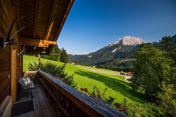 A wooden balcony with a bench, overlooking a green field and a mountain.