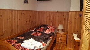 Ein Einzelbett mit floralem Überwurf, ein Nachttisch mit Lampe, ein Holzschrank und ein an der Wand montierter Fernseher.