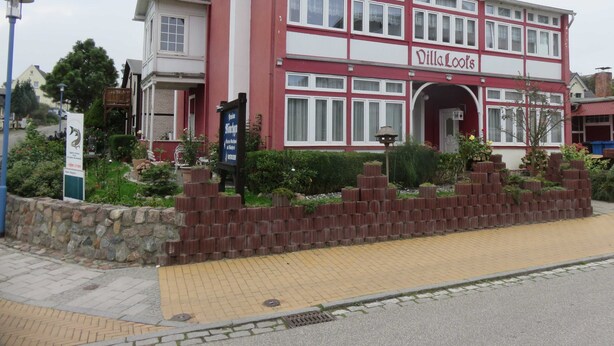 Ein rot-weißes Villa Loos Gebäude mit einer Steinmauer und einem gepflasterten Weg.