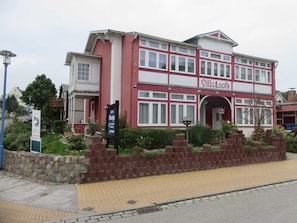 Un bâtiment de style Villa Loos aux couleurs rouge et blanche, doté d’un mur en pierre et d’un chemin piétonnier dallé.