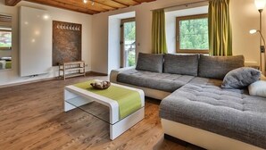 Un soggiorno moderno con soffitto in legno, un divano componibile, un tavolino bianco e vista sul verde.