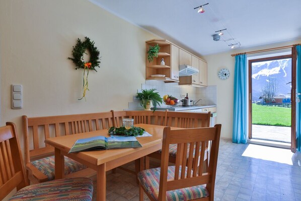 Un comedor con mesa y bancos de madera, una cocina con armarios y un ventanal, y vistas a un paisaje montañoso.