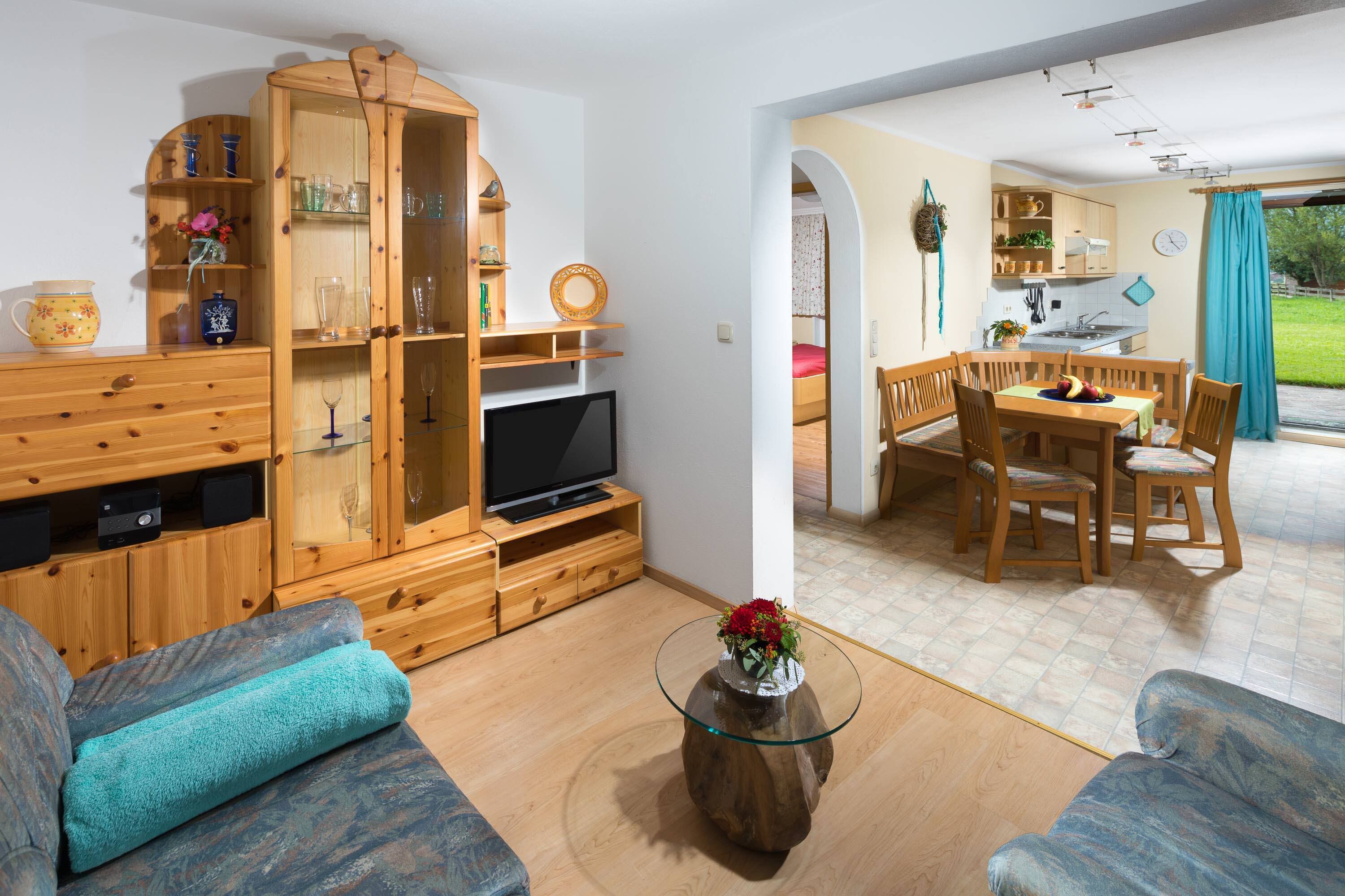 Een woonkamer met een televisie, houten meubels en een eethoek met stoelen en een tafel.