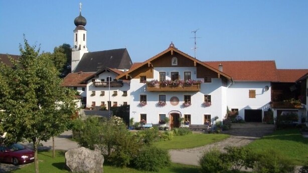 A traditional building with a balcony, a large rock in the foreground, and a clear sky. - Ferienwohnung 1 "Hortensie" (Nußdorf i. Chiemgau)