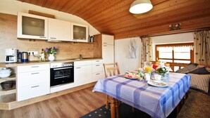 A cozy kitchen with wooden cabinets, a dining table set for two, and a window with curtains. - Ferienwohnung 1 "Hortensie" (Nußdorf i. Chiemgau)