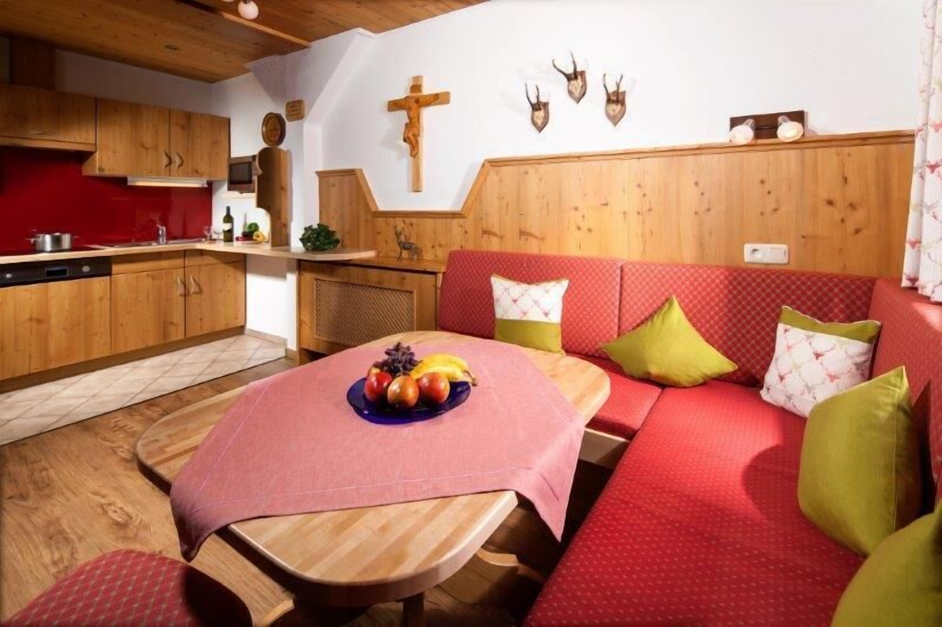 Um quarto acolhedor com uma mesa de jantar de madeira, um sofá vermelho e uma cozinha rústica com detalhes vermelhos.