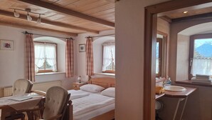 Ein Hotelzimmer mit einem hölzernen Bett, einem Schreibtisch mit Stuhl, einem Fenster mit Vorhängen, einem Badezimmer mit Waschbecken und Spiegel sowie Bergblick.