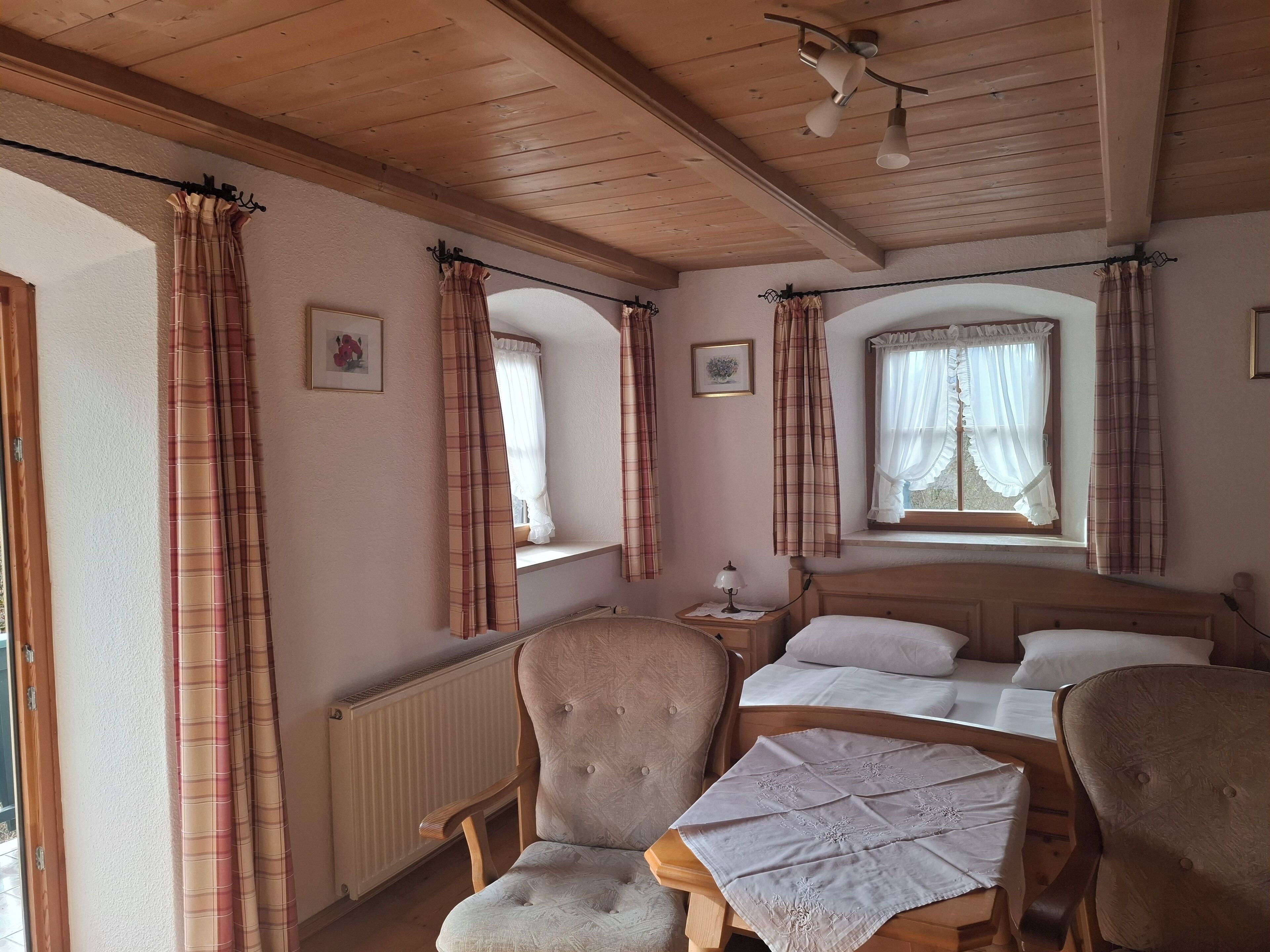 A cozy room with a bed, two chairs, a table, and a window with curtains.