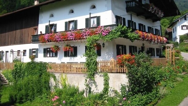 Ein zweistöckiges Gebäude mit einem Balkon, der mit bunten Blumen geschmückt ist, einer Holzzahlung und einer Bergkulisse.