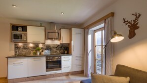 Una cocina moderna con armarios blancos, horno empotrado y microondas. Hay una ventana con cortinas y una lámpara de pared.
