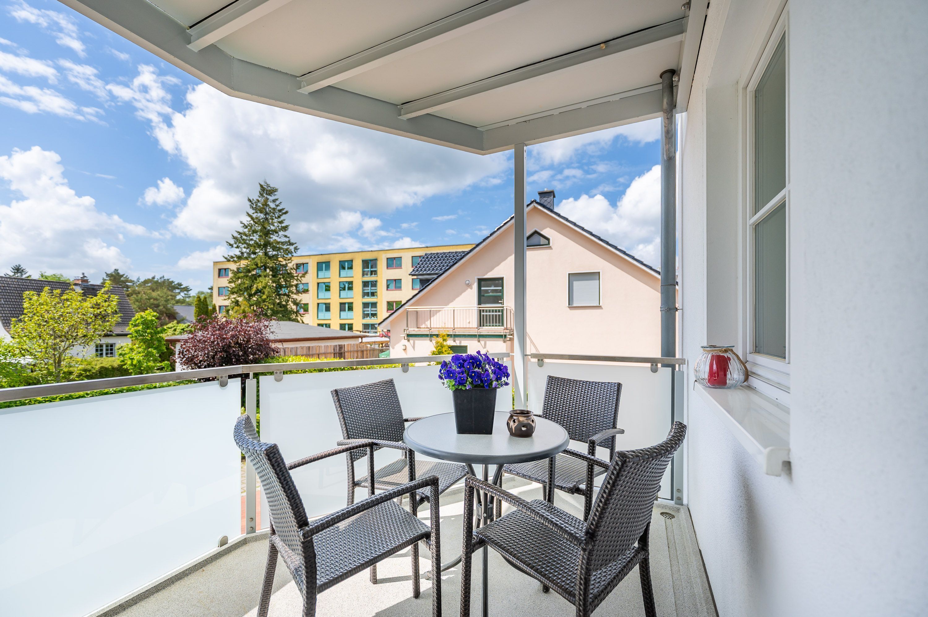 Ein Balkon mit Korbstühlen, einem Tisch und einem Blumentopf.