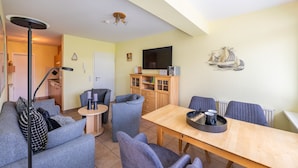 Un espace de vie compact comprenant un canapé, des fauteuils, une table à manger, un téléviseur et un meuble.