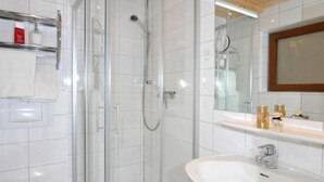 Ett modernt badrum med en dusch som är avskärmad med glasväggar, ett vitt handfat och en toalett.