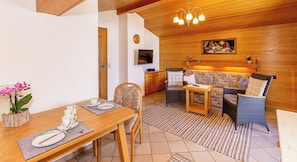 Un salon chaleureux avec un plafond en bois, un ensemble de canapés, une table à manger avec des chaises et un téléviseur fixé au mur.