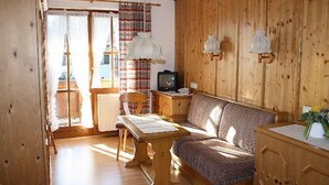 Et hyggeligt værelse med en træseng, et træskrivebord, et fjernsyn og et vindue med gardiner.