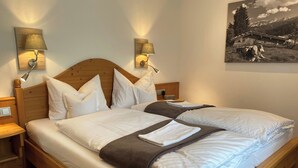 Uma cama de casal com lençóis brancos, duas mesas de cabeceira e luminárias fixadas na parede.