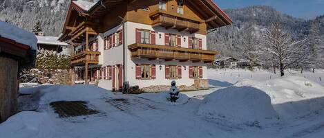 A multi-story chalet with wooden balconies, set in a snowy mountainous area.