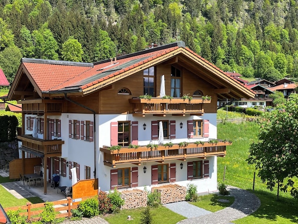 A two-story chalet with wooden balconies, a red-tiled roof, and a stone foundation.