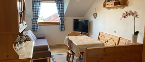A cozy room with a bed, a sofa, a TV, and a wooden shelf with decorative items.