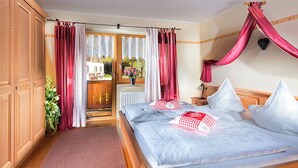 A bedroom with a large bed, wooden wardrobe, and a view of a garden through a glass door. - Vacation apartment Morgensonne, for 1-4 persons (Berchtesgaden)