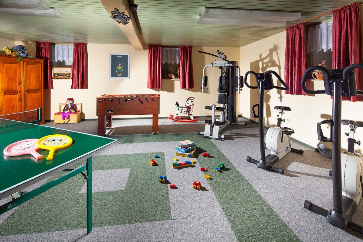 Una habitación con mesa de ping pong, equipo de ejercicios y mesa de fútbolín.