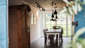 A dining area with a wooden table and chairs, a large window with a view of greenery, and pendant lighting. - Ferienwohnung II "Kampen" 57 qm, extra Schlafzimmer und Balkon (Aschau im Chiemgau)