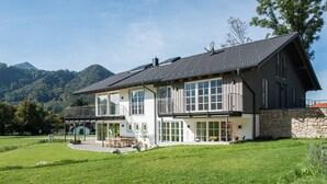 A two-story house with a balcony, large windows, and a stone wall. - Ferienwohnung II "Kampen" 57 qm, extra Schlafzimmer und Balkon (Aschau im Chiemgau)