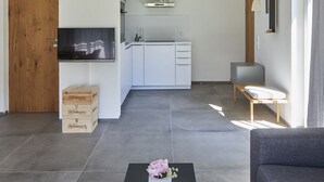 A spacious living area with a high ceiling, a wooden staircase, a kitchen with white cabinets, a flat-screen TV, and a grey sofa. - Ferienwohnung II "Kampen" 57 qm, extra Schlafzimmer und Balkon (Aschau im Chiemgau)
