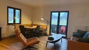 A modern living room with a wooden floor, a leather chair, a dining table with chairs, a coffee table, and a sofa. - Apartment Anemone for 3 persons, balcony, 1 bedroom, 46 m² (Inzell)