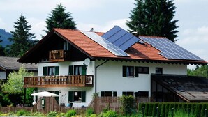 A two-story house with a balcony, solar panels on the roof, and a fenced garden area. - Apartment Anemone for 3 persons, balcony, 1 bedroom, 46 m² (Inzell)