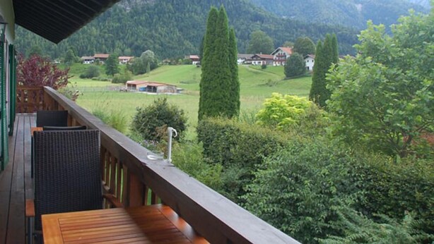 A balcony with a wooden floor, a metal railing, and a view of a mountainous landscape with houses and greenery. - Apartment Anemone for 3 persons, balcony, 1 bedroom, 46 m² (Inzell)