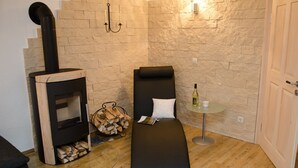 Una habitación pequeña con pared de piedra, un sofá negro, una mesa con una botella y un estufa de leña.