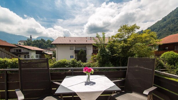 A dining area with a table and chairs, a vase with flowers, and a view of houses and mountains. - Apartment Westernberg 35 sqm, 1 living/bedroom, kitchen, balcony, max. 2 p. (Ruhpolding)