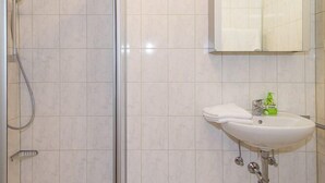 A bathroom with a shower, a sink with a mirror, and tiled walls. - Apartment Westernberg 35 sqm, 1 living/bedroom, kitchen, balcony, max. 2 p. (Ruhpolding)