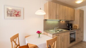 A compact kitchen with wooden cabinets, a stainless steel sink, and a built-in oven. - Apartment Westernberg 35 sqm, 1 living/bedroom, kitchen, balcony, max. 2 p. (Ruhpolding)