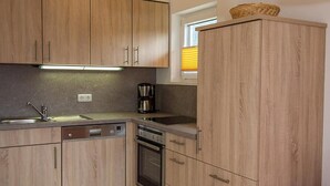 A kitchen with wooden cabinets, a dishwasher, an oven, and a coffee maker. - Apartment Westernberg 35 sqm, 1 living/bedroom, kitchen, balcony, max. 2 p. (Ruhpolding)