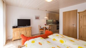 A bedroom with a bed, a TV, a desk, and a kitchenette. - Apartment Westernberg 35 sqm, 1 living/bedroom, kitchen, balcony, max. 2 p. (Ruhpolding)