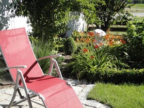 Una silla roja en un jardín con un muro blanco y un árbol al fondo.