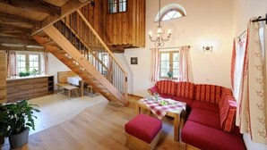 A wooden staircase leading to an upper level, a red sofa set, a dining table with a checkered tablecloth, and a chandelier. - Ferienwohnung "Tegernsee", 90 qm Obergeschoss, 3 separate Schlafzimmer (Höslwang)