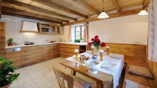 A cozy kitchen with wooden beams, a microwave, and a dining table set for two with beer glasses and a vase of flowers. - Ferienwohnung "Tegernsee", 90 qm Obergeschoss, 3 separate Schlafzimmer (Höslwang)