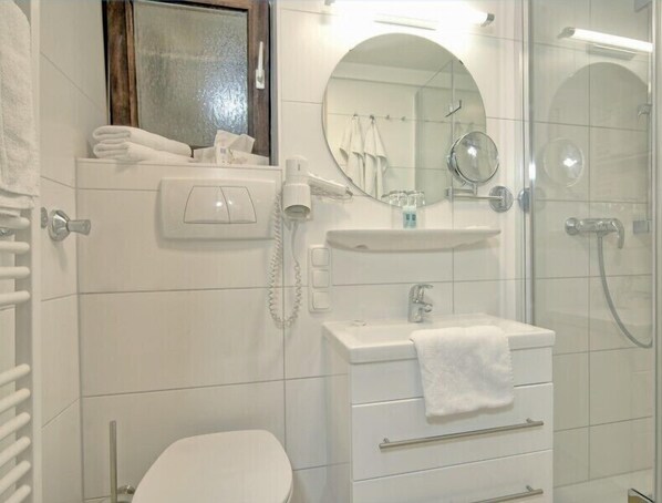 Een moderne badkamer met toilet, wastafel met spiegel, douche en handdoekhouder.