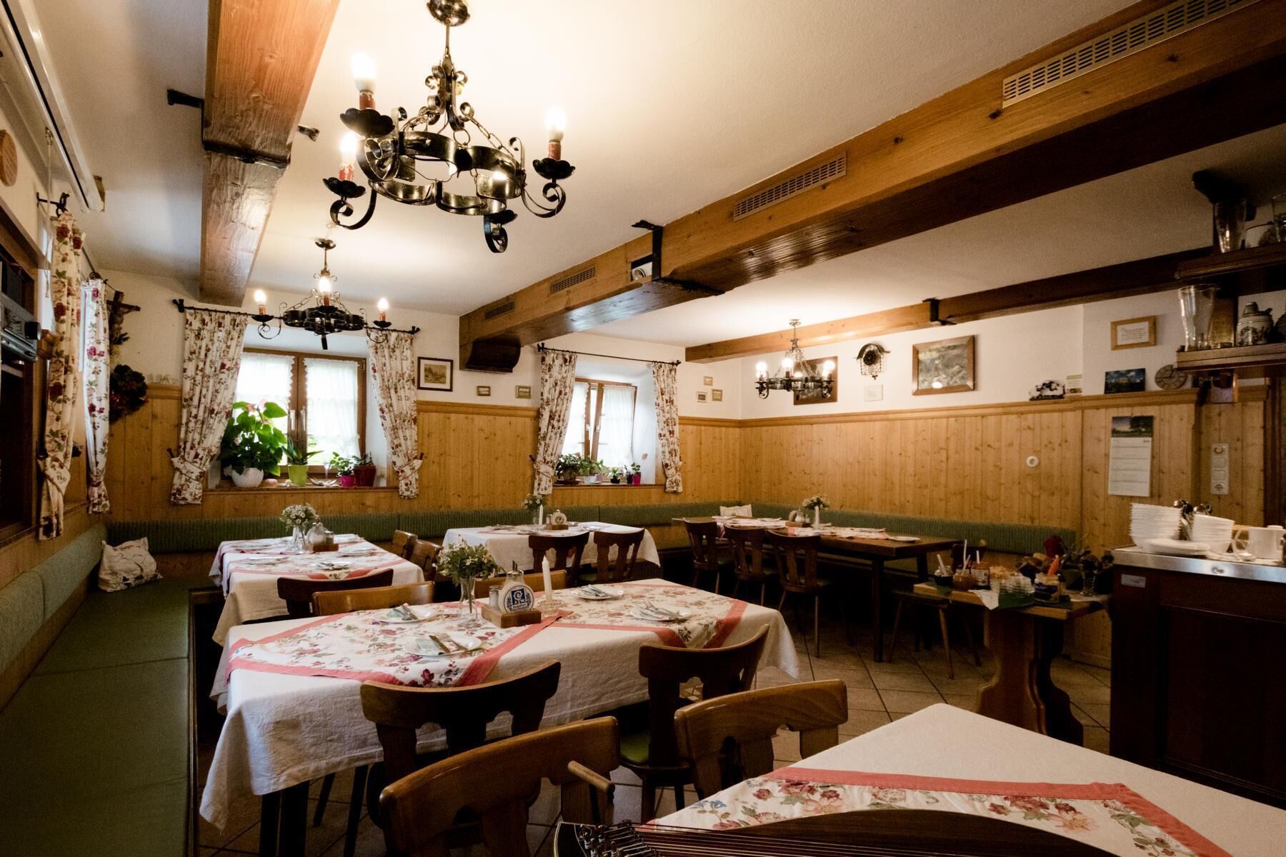 A cozy restaurant with wooden paneling, floral curtains, and multiple tables set for dining.