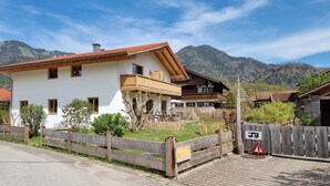 Un chalet à deux étages doté d’un balcon, entouré d’une clôture en bois et avec une vue sur les montagnes en toile de fond.