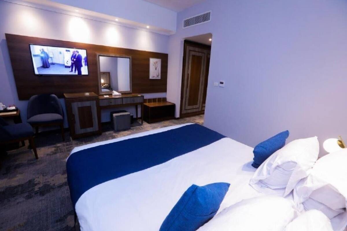 A hotel room with a large bed, a desk, a chair, a television, and a door.
