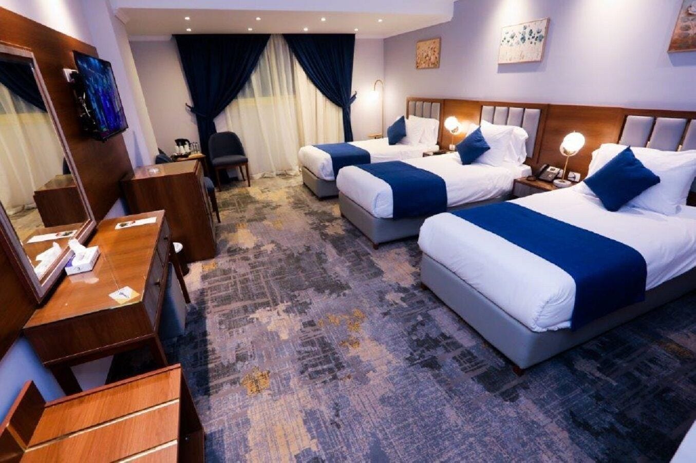A hotel room with two beds, a desk, a chair, a TV, and a large window with curtains.