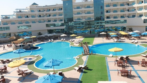 Un hôtel doté de plusieurs piscines, de chaises longues, de parasols et d’un grand bâtiment avec des balcons.