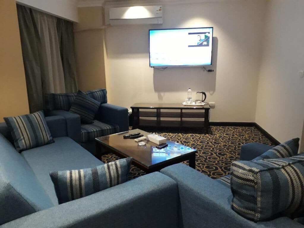 Ein Hotelzimmer mit einer Sofagarnitur, einem Couchtisch, einem an der Wand befestigten Flachbildfernseher und einem gemusterten Teppich.