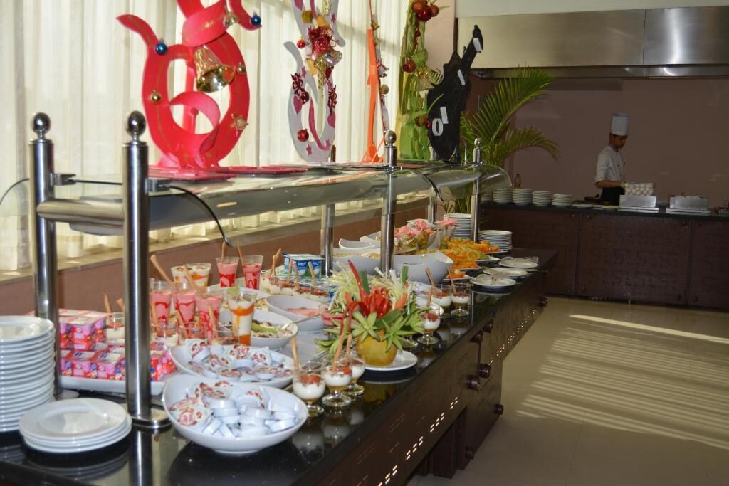 Montaje tipo buffet con diferentes opciones de comida y bebidas, un chef al fondo y elementos decorativos en la pared.
