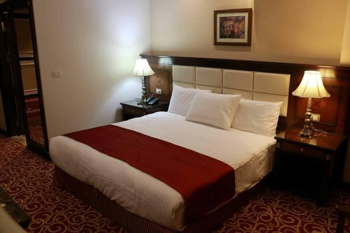 A hotel room with a large bed, two bedside tables, a red carpet, and a framed picture on the wall.